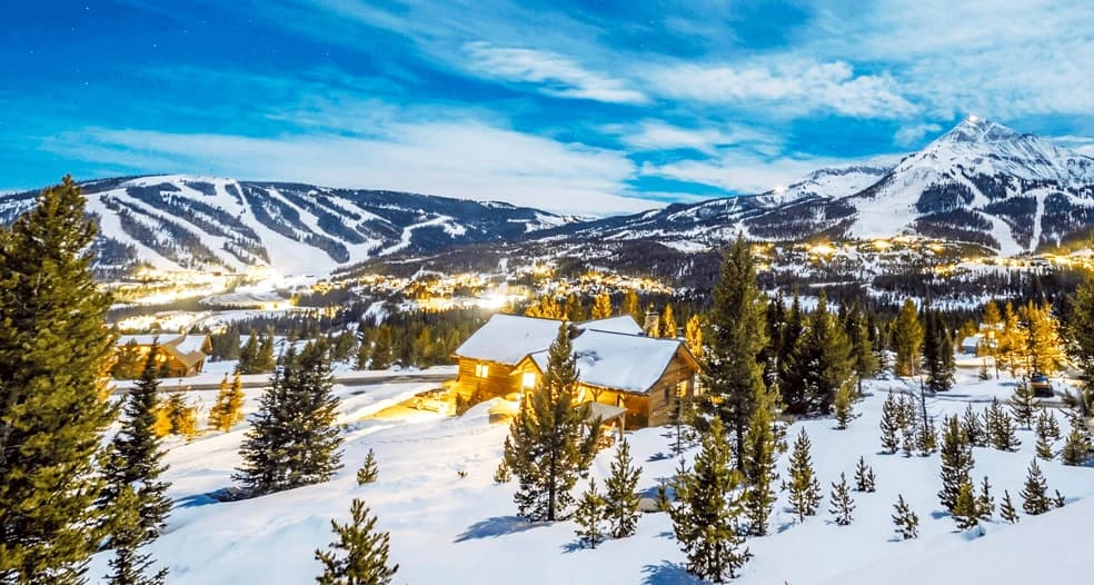 Big Sky Montana ski resort 2026 - aerial daytime view of Lone Peak summit at 11,166 feet with fresh powder snow, 40 ski lifts across 5,850 acres, mountain village base with luxury lodges, groomed ski runs, blue Montana sky, and gateway access to Yellowstone National Park winter activities