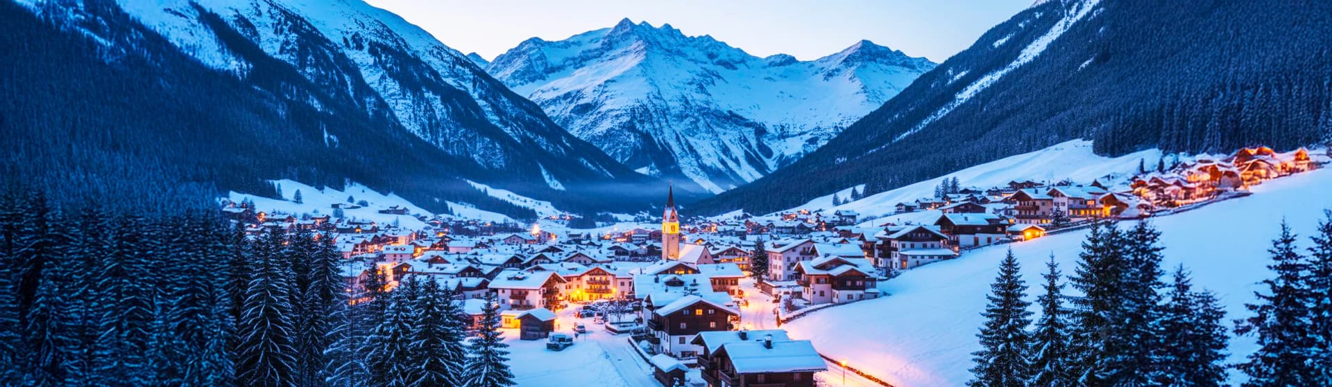 Austrian Alps ski resort village at dusk 2025 - traditional Tyrolean chalets and hotels with warm lighting nestled in snow-covered valley, surrounded by dramatic mountain peaks, pine forests, and pristine ski slopes in winter