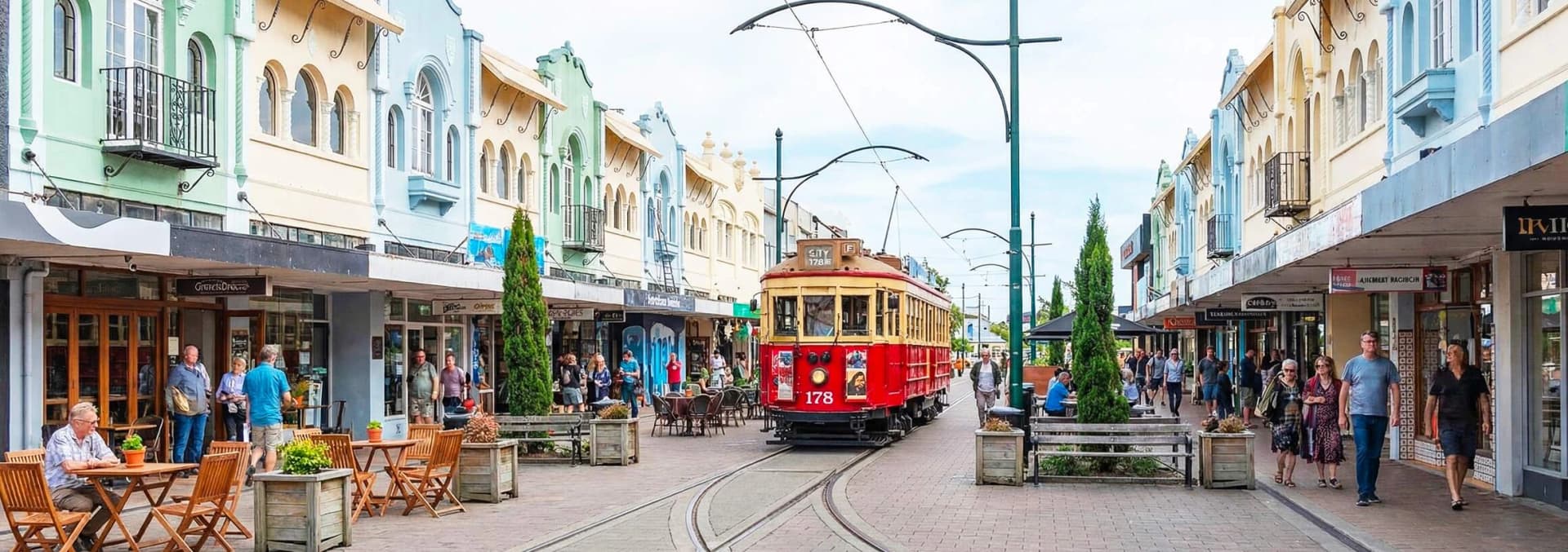 Historic Christchurch tram number 178 on New Regent Street - iconic red and cream heritage tramway passing colorful Spanish Mission style buildings, outdoor cafes with tourists, and boutique shops in Christchurch central city pedestrian precinct New Zealand
