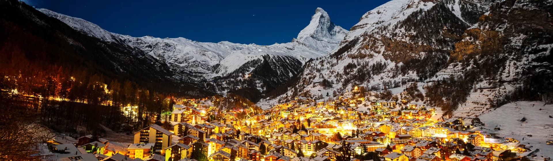 Zermatt Switzerland in December 2025 featuring the iconic pyramid-shaped Matterhorn mountain peak covered in snow towering over traditional Swiss alpine chalets and timber buildings in the car-free village, showcasing world-class skiing destination with pristine powder snow and luxury ski resort atmosphere in the Swiss Alps