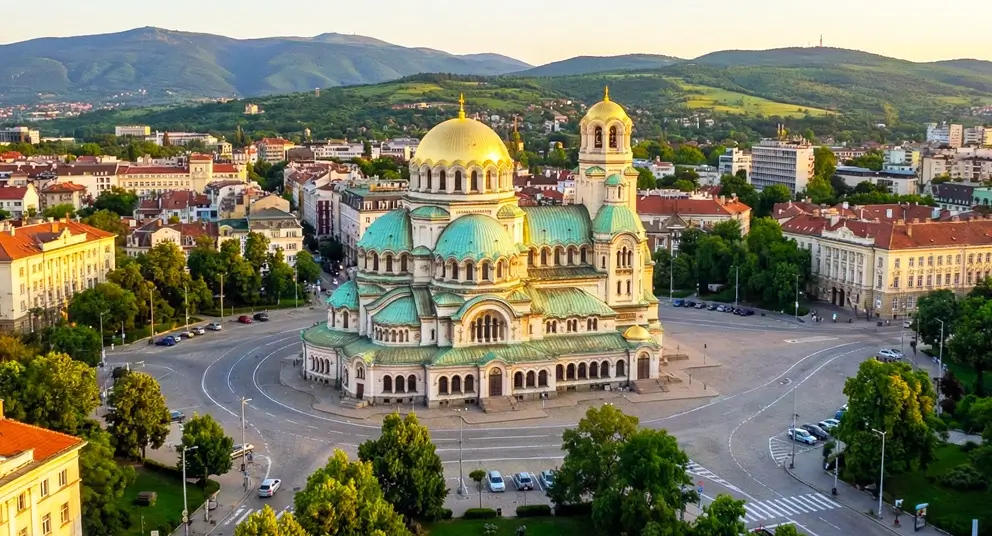 Sofia Bulgaria travel guide 2026 - stunning aerial view of Alexander Nevsky Cathedral with iconic golden dome and green copper rooftops surrounded by historic city center buildings, tree-lined boulevards, and Vitosha Mountain backdrop at golden hour, showcasing Europe's most affordable capital for budget travelers
