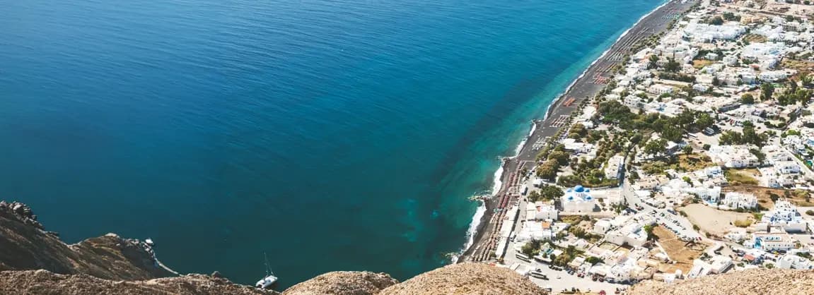 Perissa Beach Santorini 2026 - long black volcanic sand beach with Mesa Vouno mountain backdrop, beach bars and clubs, budget-friendly hotels, backpacker atmosphere, and crystal clear Aegean Sea waters