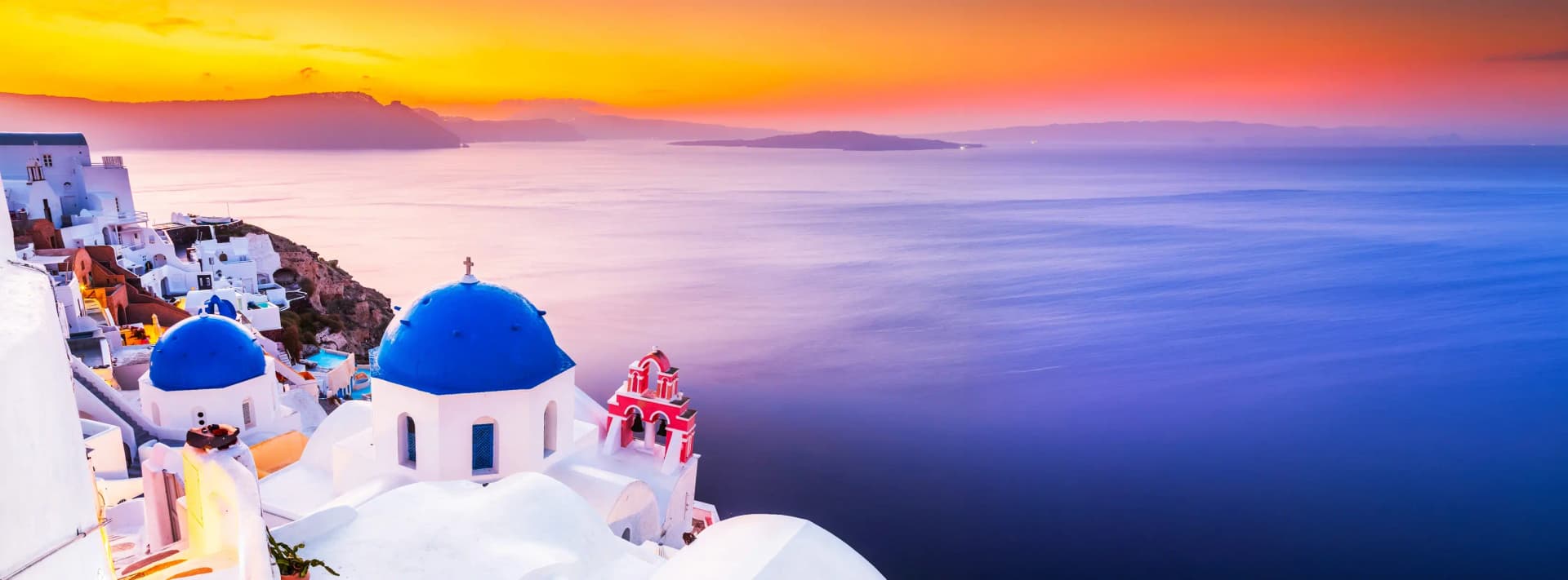 Where to stay in Santorini 2026 - stunning panoramic view of whitewashed buildings with blue domes overlooking the volcanic caldera at golden hour, iconic Cycladic architecture, luxury cave hotels with private pools, and the deep blue Aegean Sea