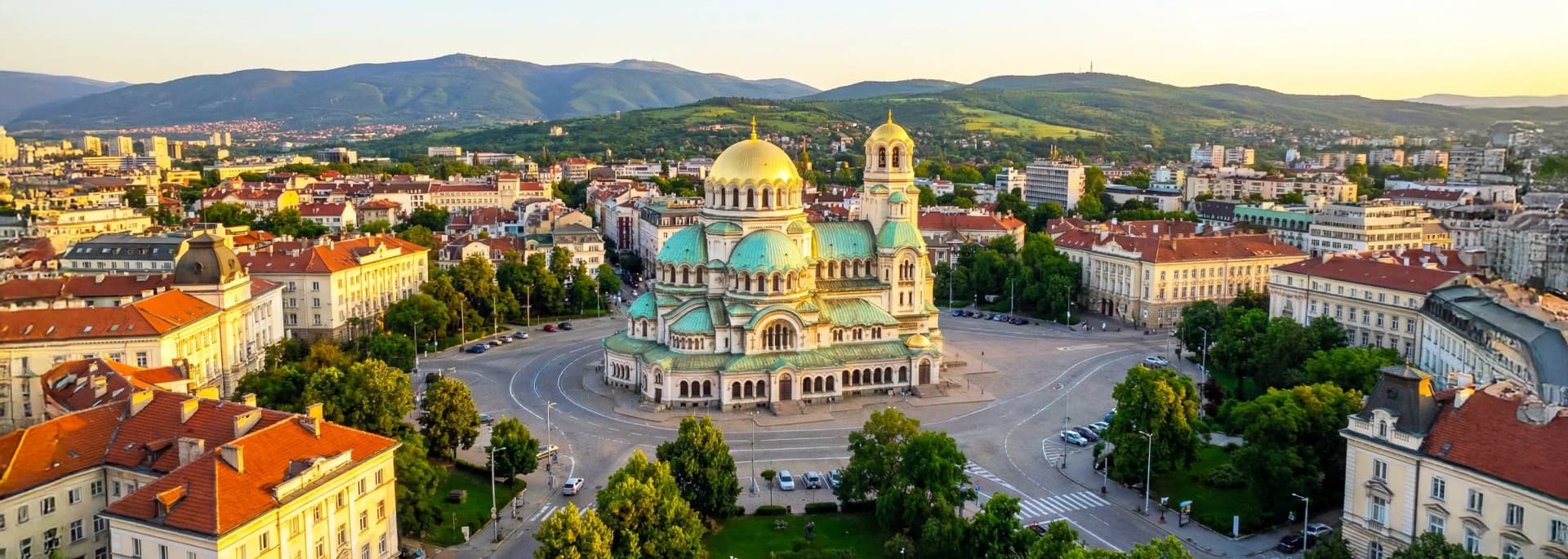 Sofia Bulgaria travel guide 2026 aerial panorama - Alexander Nevsky Cathedral golden domes, Vitosha Mountain backdrop, historic city center with terracotta rooftops, tree-lined boulevards at golden hour - Europe's cheapest capital for budget travelers with hotels from €34 per night