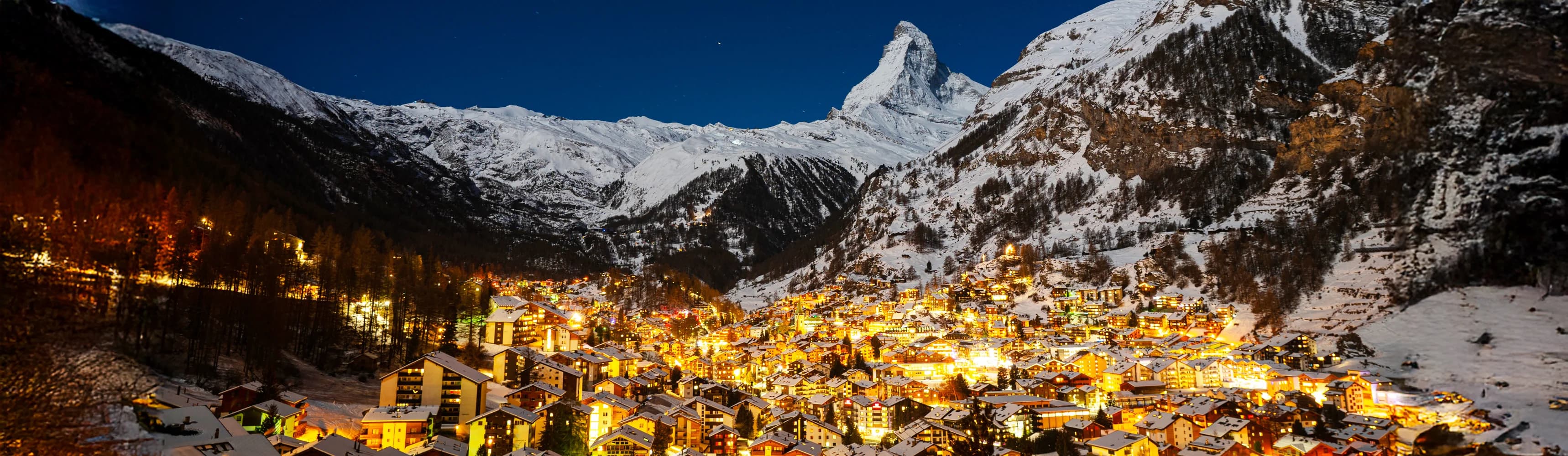 Zermatt Switzerland ski resort with iconic Matterhorn mountain peak at sunset - traditional wooden chalets and luxury hotels with warm lighting in car-free alpine village, snow-covered ski slopes, pine forests, and dramatic Swiss Alps peaks perfect for winter skiing vacation 2025